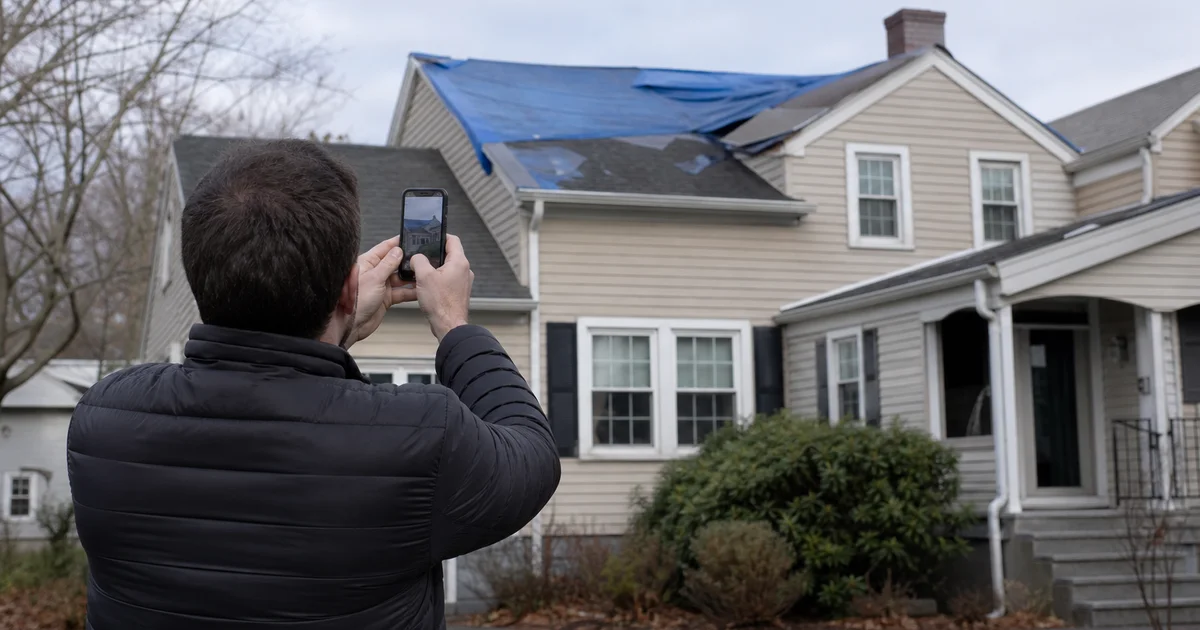 Homeowner photographing roof storm damage with phone for insurance documentation